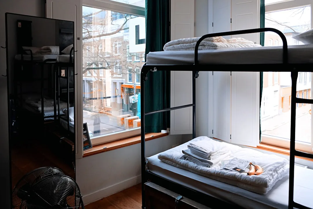 Sauberes modernes Hostel-Zimmer mit schwarzem Metallstockbett und Stadtblick aus dem Fenster