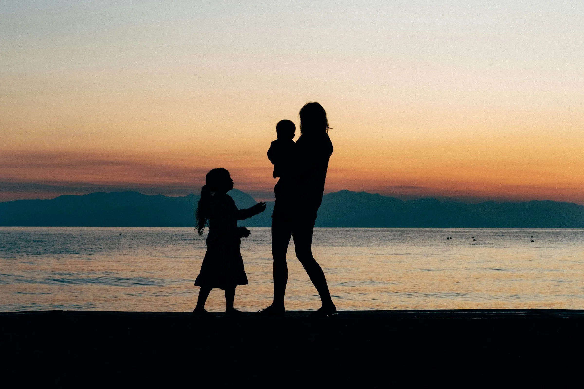 Mother with two children walking on a sandy beach at sunrise in Corfu, Greece