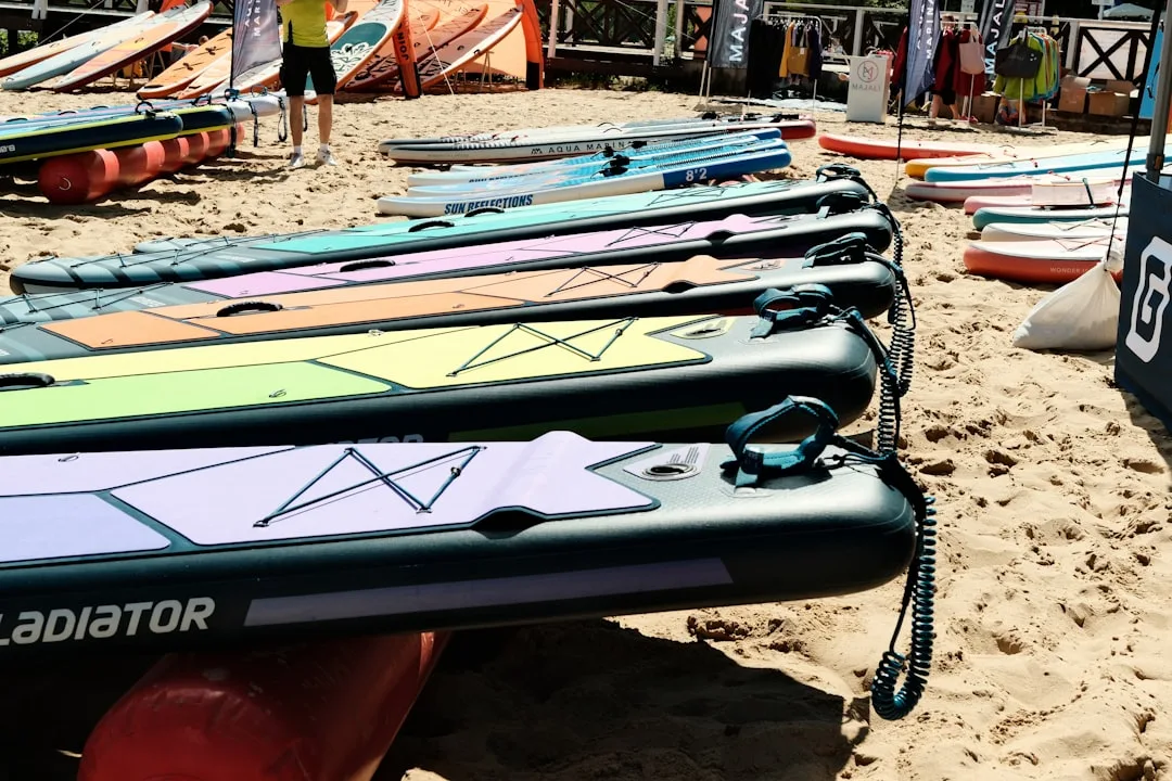 Colorful inflatable SUP boards lined up on a sandy beach by the sea