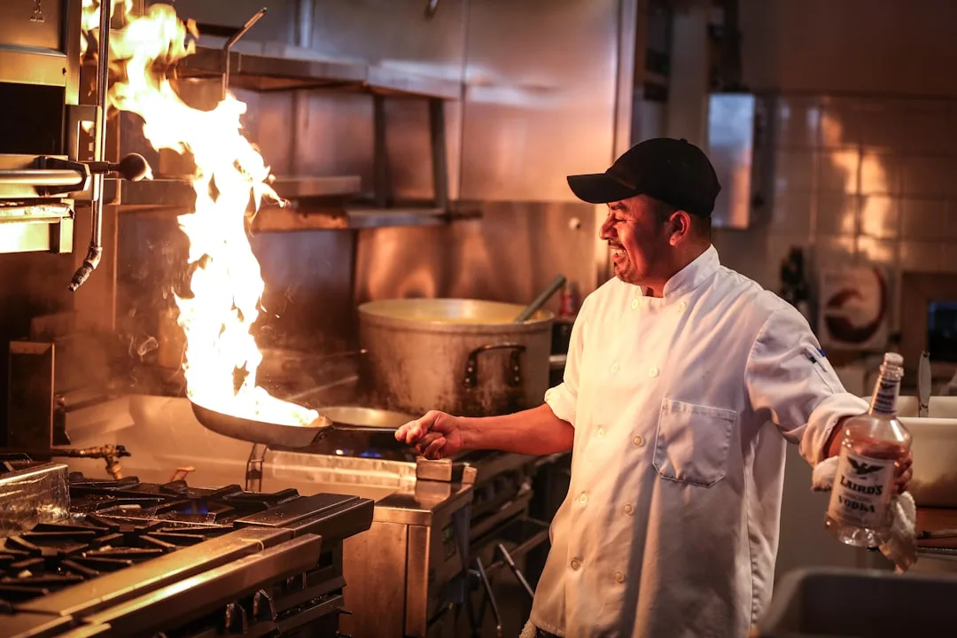 Sternekoch im weißen Kittel kocht mit einer Flamme in der Restaurantküche