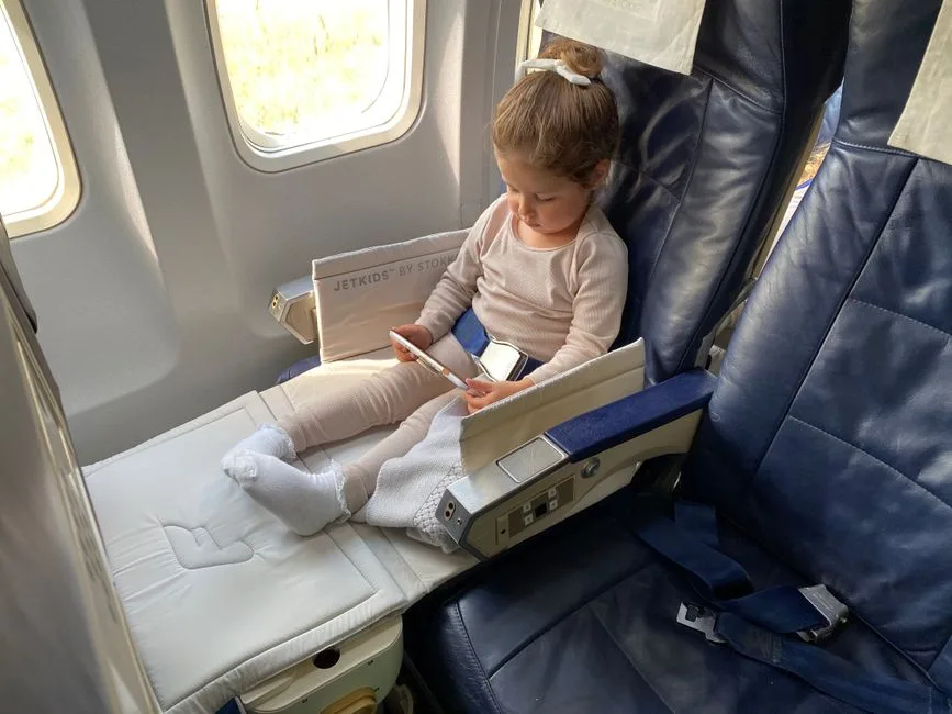 Little girl sitting on an airplane seat entertained by a tablet device