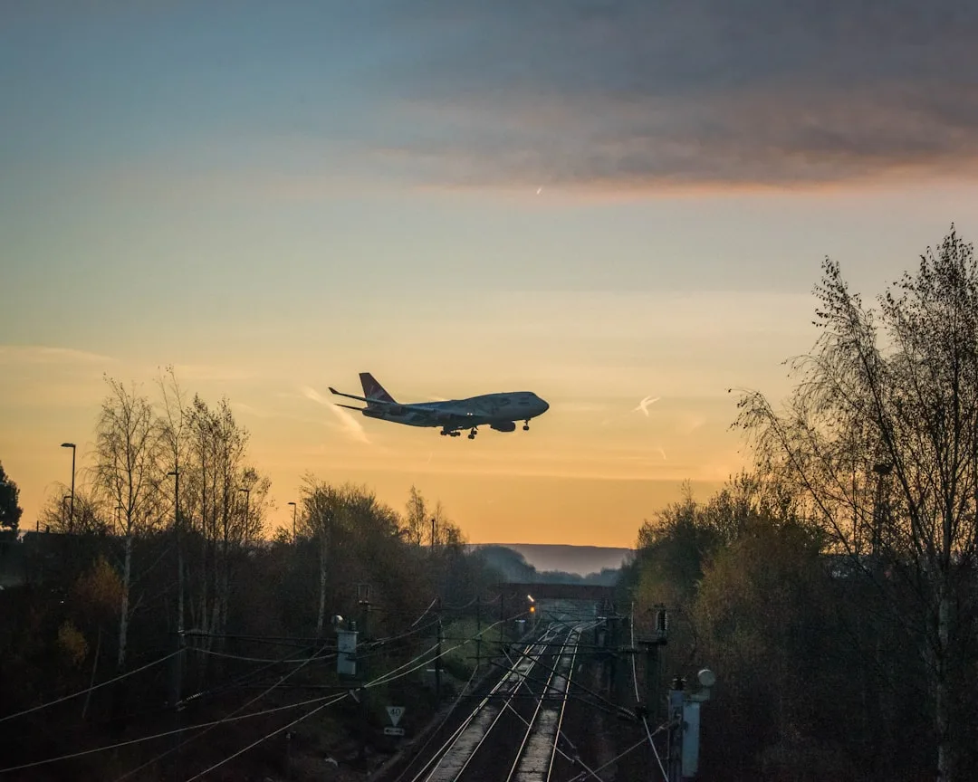 Flugzeug landet bei Sonnenuntergang über Bahngleisen – Vergleich von Flugreise und Bahnfahrt im CO2-Fußabdruck