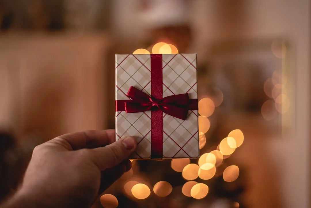 Hand hält ein kleines Geschenk mit roter Schleife vor warmem Bokeh-Hintergrund — Reisegutschein