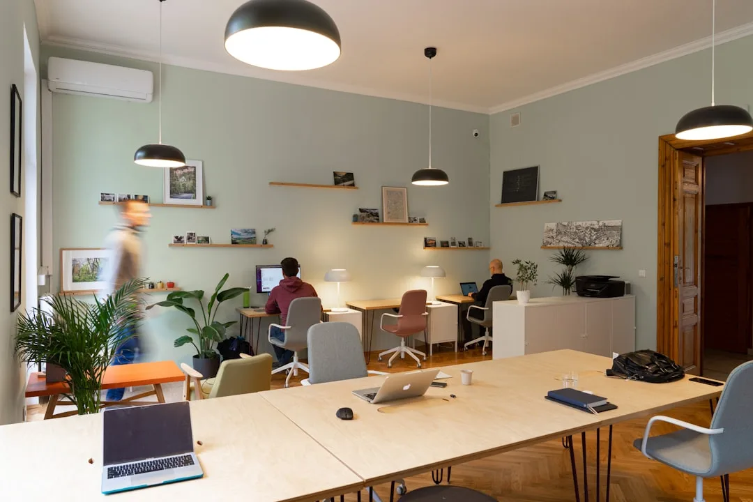 Heller offener Coworking-Space mit langen Holztischen, Hängeleuchten und Personen, die an Laptops arbeiten