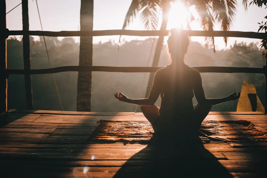 Woman meditating on a wooden dock in a tropical setting at sunset