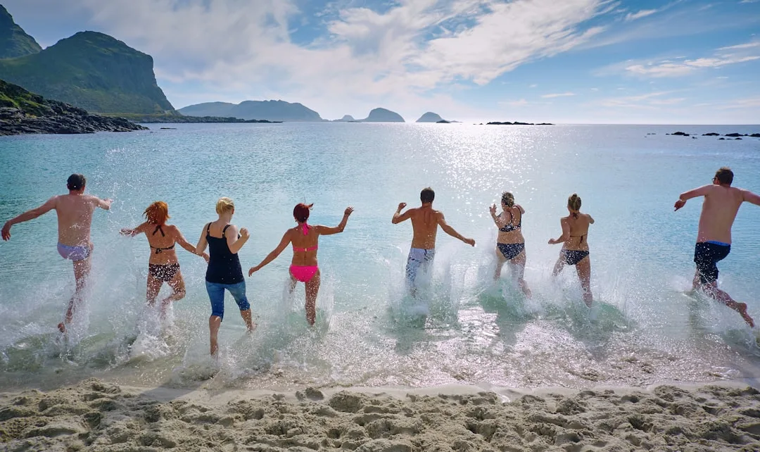 Jugendliche springen gemeinsam ins Meer an einem sonnigen Strand