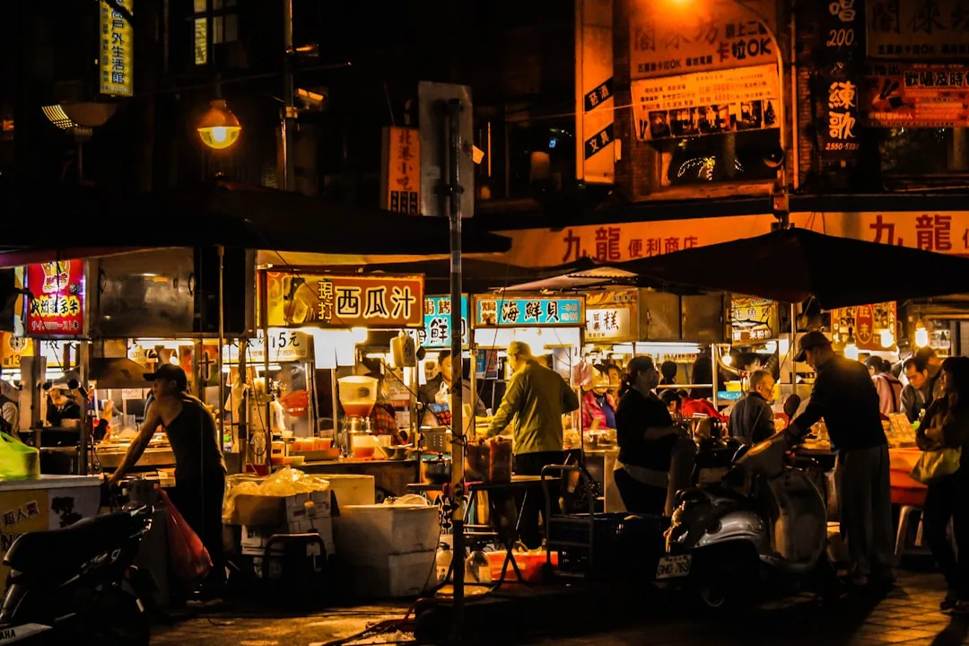 Belebter asiatischer Straßenmarkt bei Nacht mit beleuchteten Essensständen und Menschen